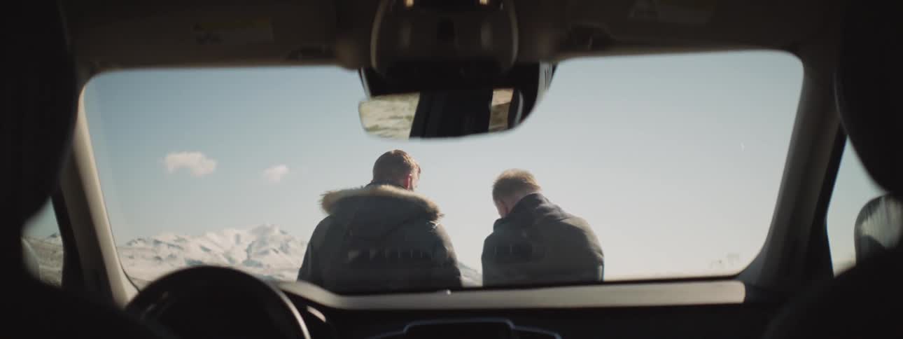 Two men stand in front of a parked car