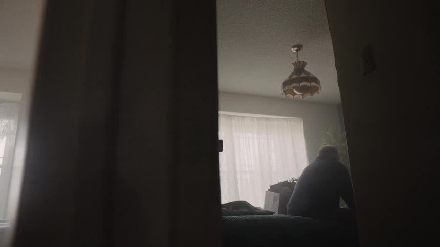 The man is sitting alone in the bedroom down the hall