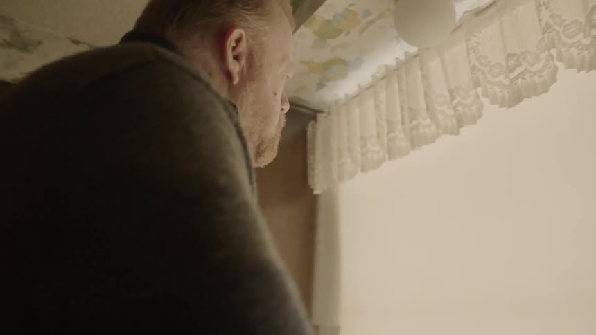Man wearing a sweater stands at the kitchen sink and stares ahead