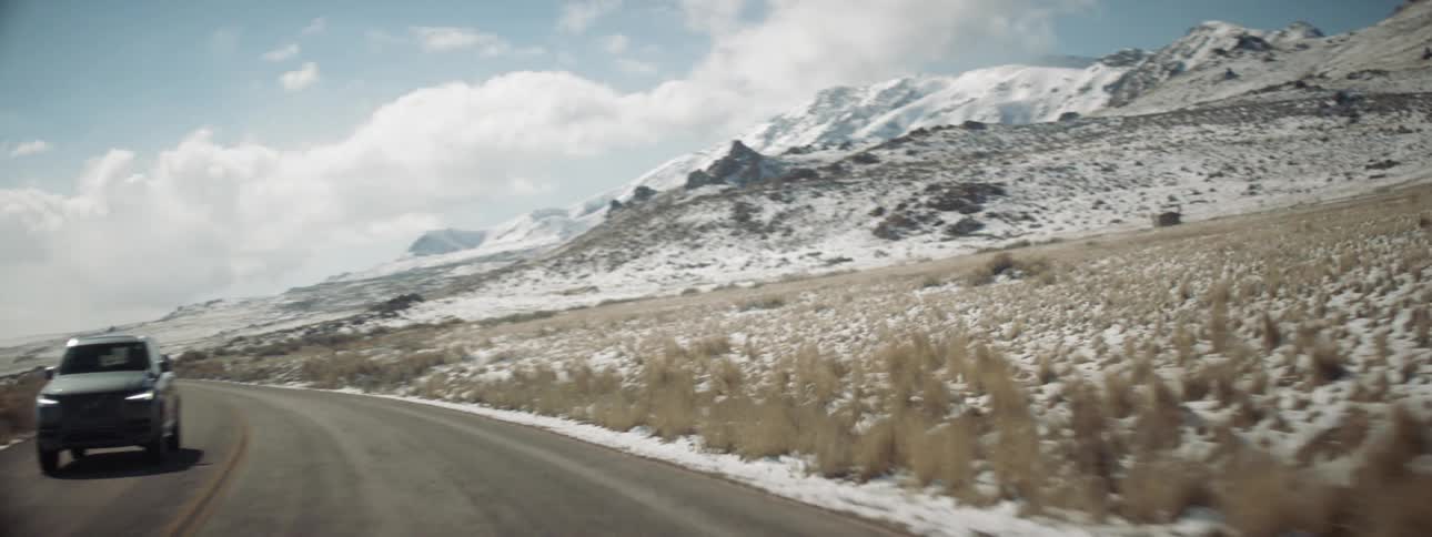 Car driving down a highway with snow on the grass and clouds overhead