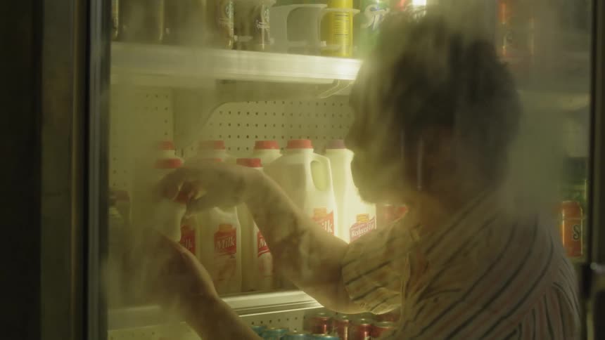 A man is checking the dates on milk in the store fridge