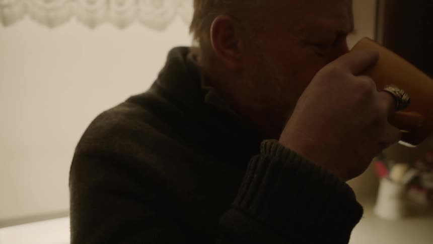 A man drinks from a mug in the dark kitchen