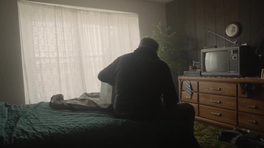 Man sits on a bed next to a cardboard box