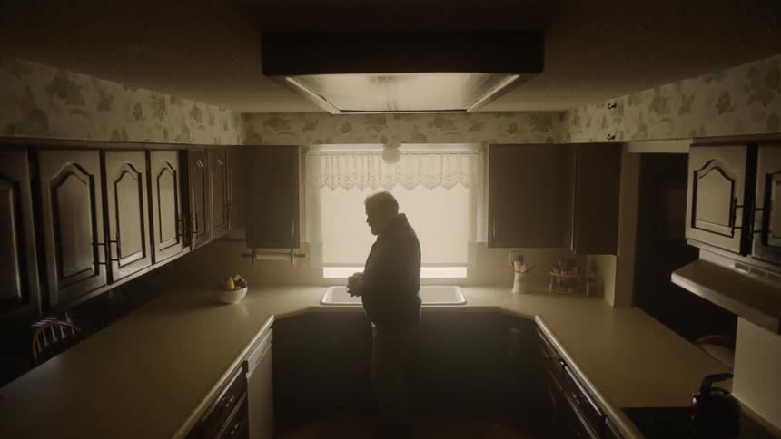 A man turns around in his kitchen holding a mug