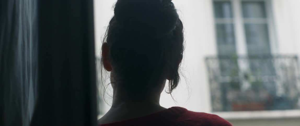 Woman leans against a wall and looks at the building across from her