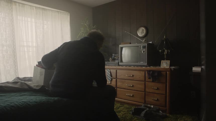 A man sits in bed looking through a cardboard box