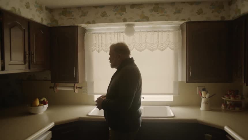 A man stands by his sink holding a cup