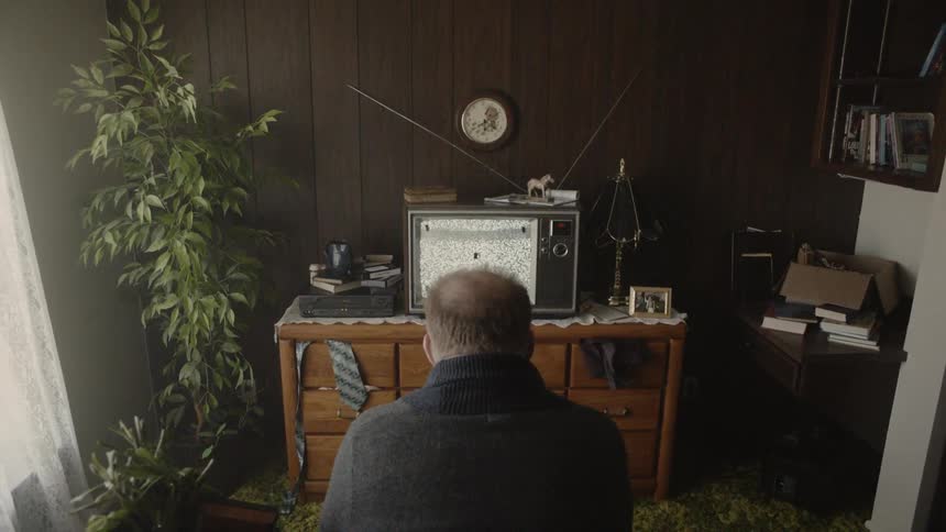 A man sits in front of the static filled television