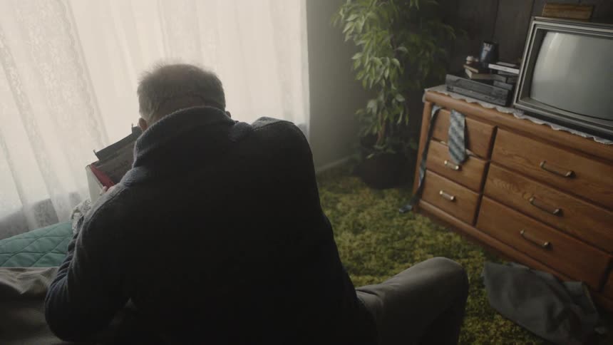 Man sits on a bed unpacking thing from a box
