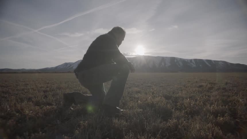 A man is crouched on a long windy field