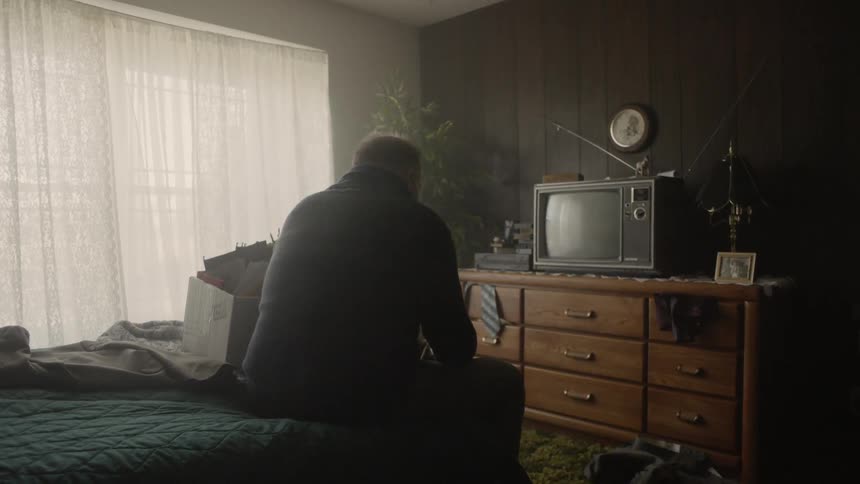 Man sits on the edge of a bed looking down
