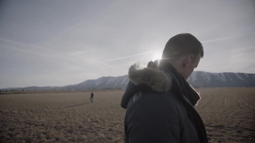 A man stands in a rural field near mountains