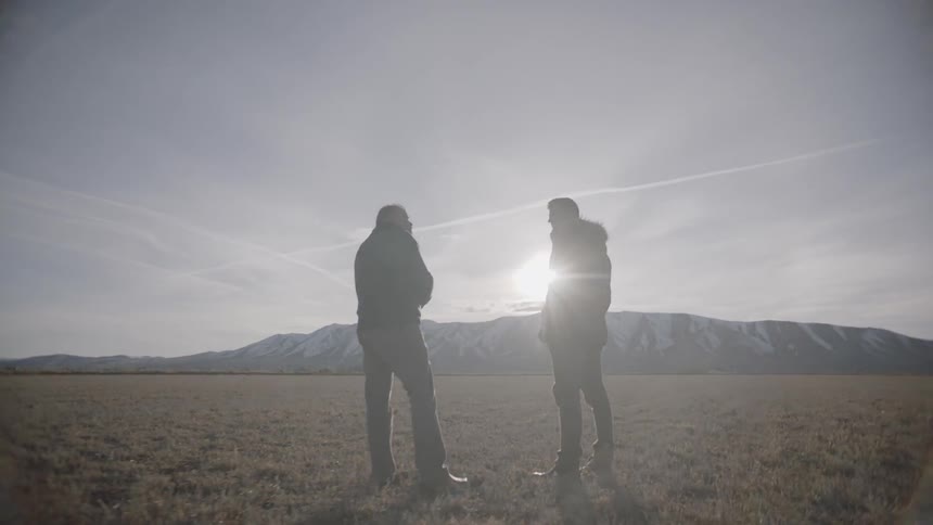 Two men stand in a large field on a sunny day