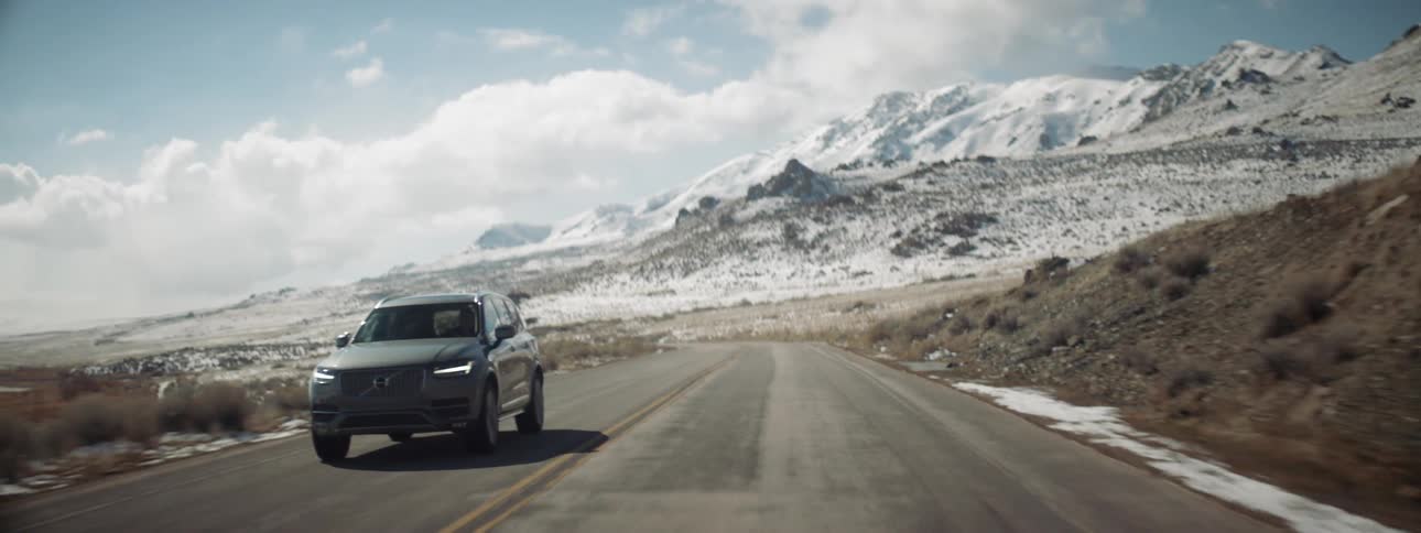 An suv travels on a rural road with snow covered peaks behind it