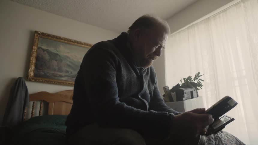 Man cries while looking at at framed photos on a bed