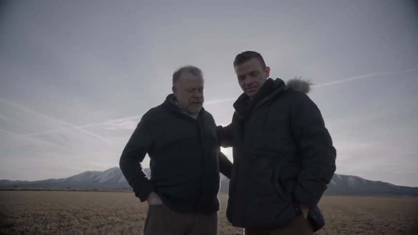 Two men talk in a rural field at sunset