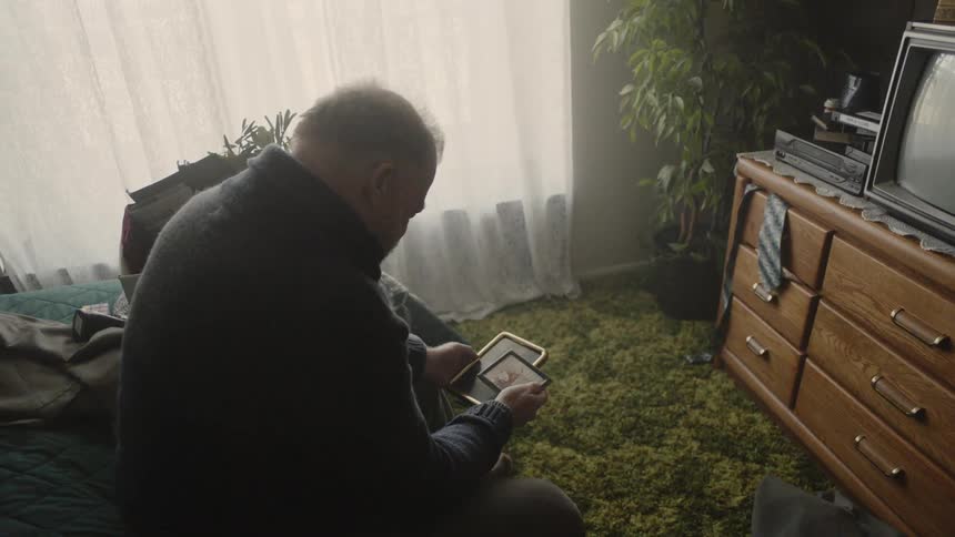 Man looks at framed photographs in a bedroom
