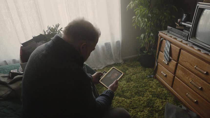 The man is sitting on his bed looking at a photo