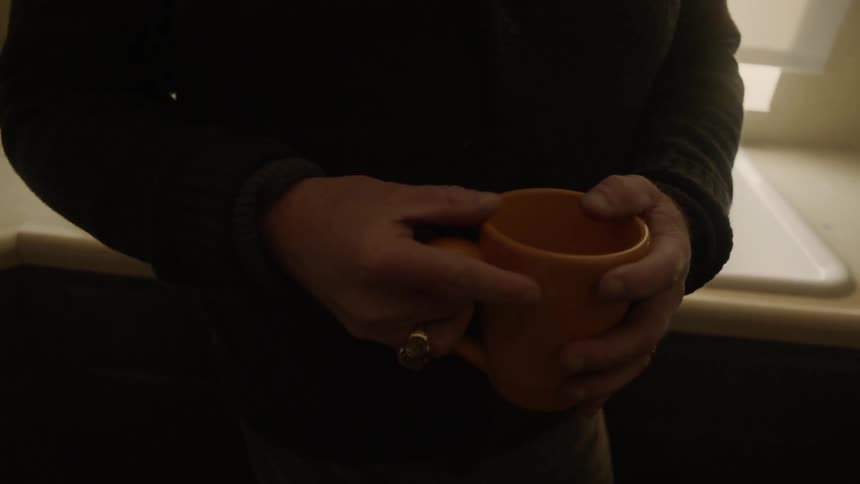 A man leans against the kitchen counter holding a mug