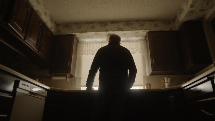 A man is standing in the dark kitchen alone