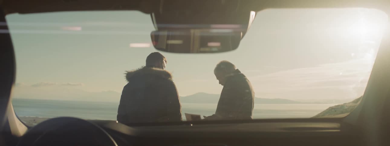 Two men stand together in front of the car
