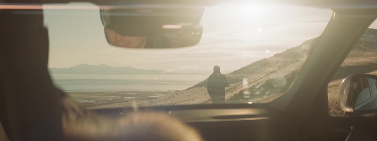 Man stands in front of a parked car at sunset