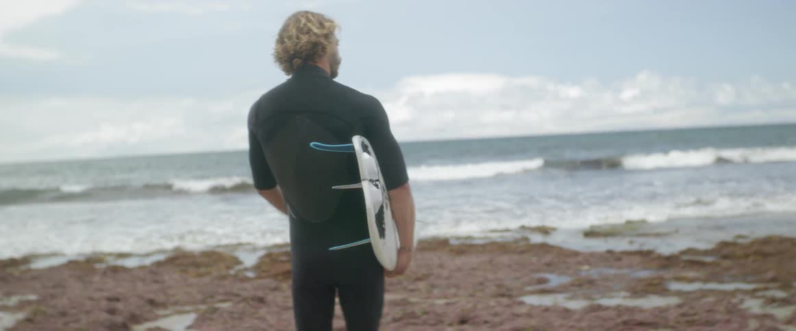 A man with a surfboard plays with his dog on the beach