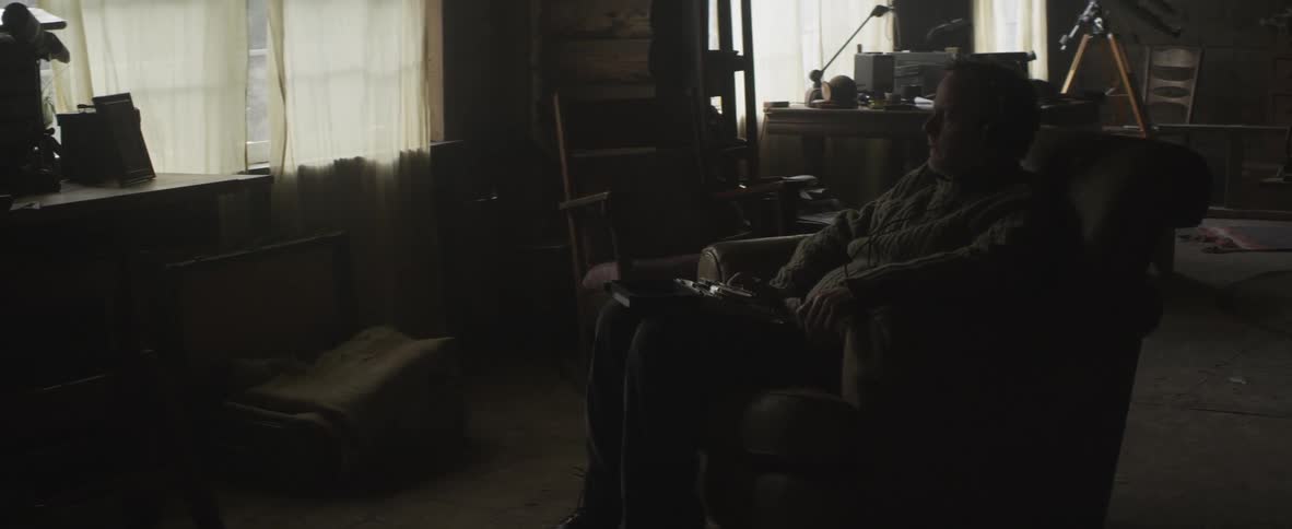 A man sits in a recliner in a darkened room and looks out the window