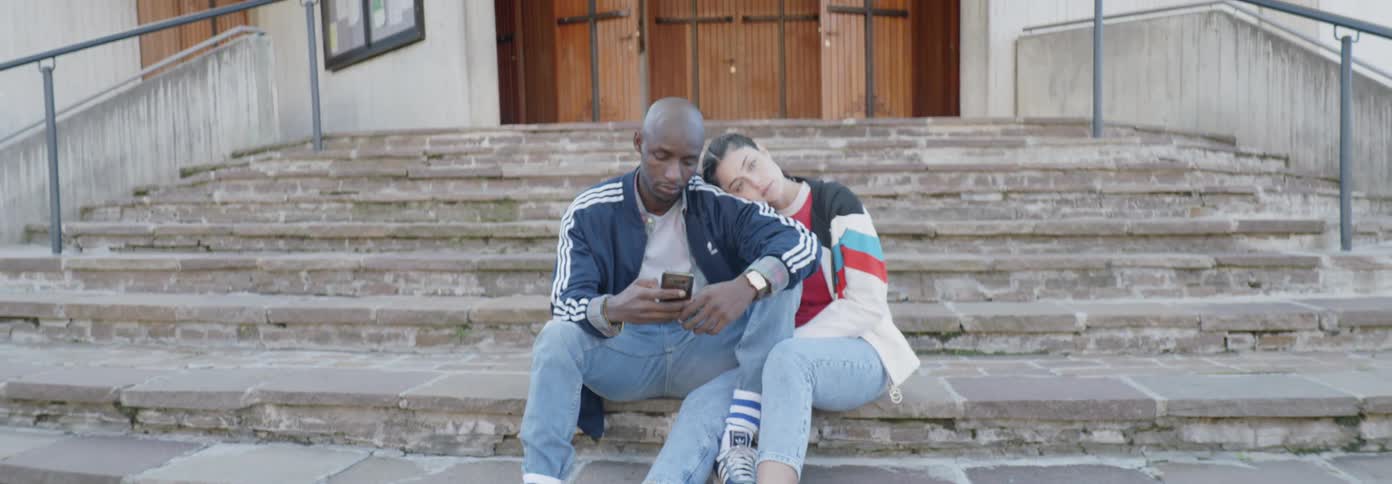 A woman leans on a man's shoulder that is using a phone