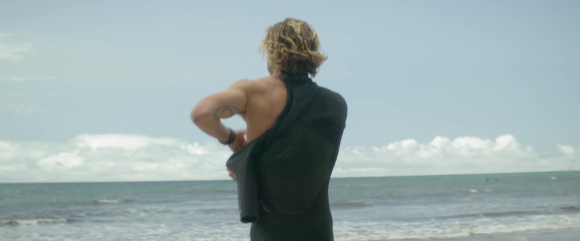 The man is putting on his wetsuit on the beach