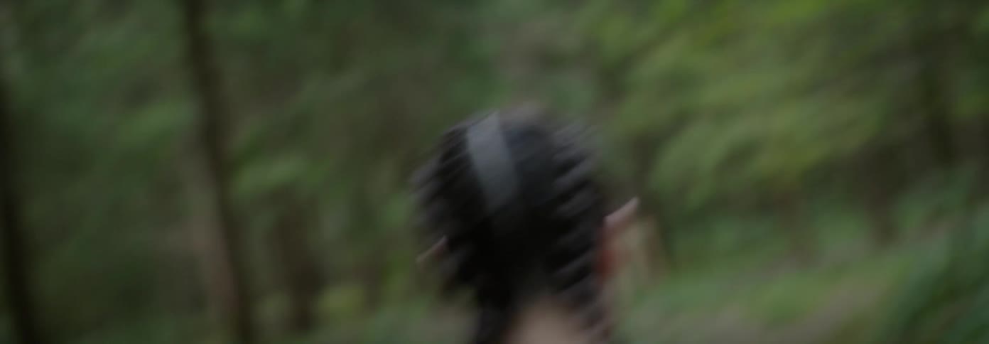 Woman runs through a forest as she looks behind her in fear