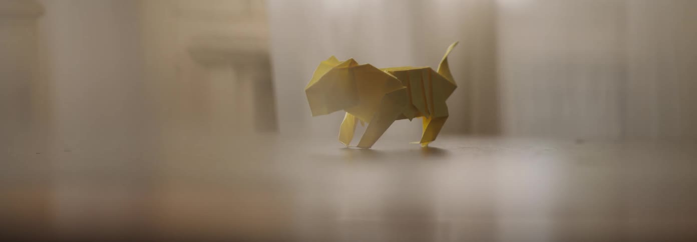 An origami figure sits on the table top as curtains billow nearby