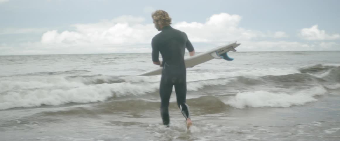 A man wades into the ocean carrying a surfboard