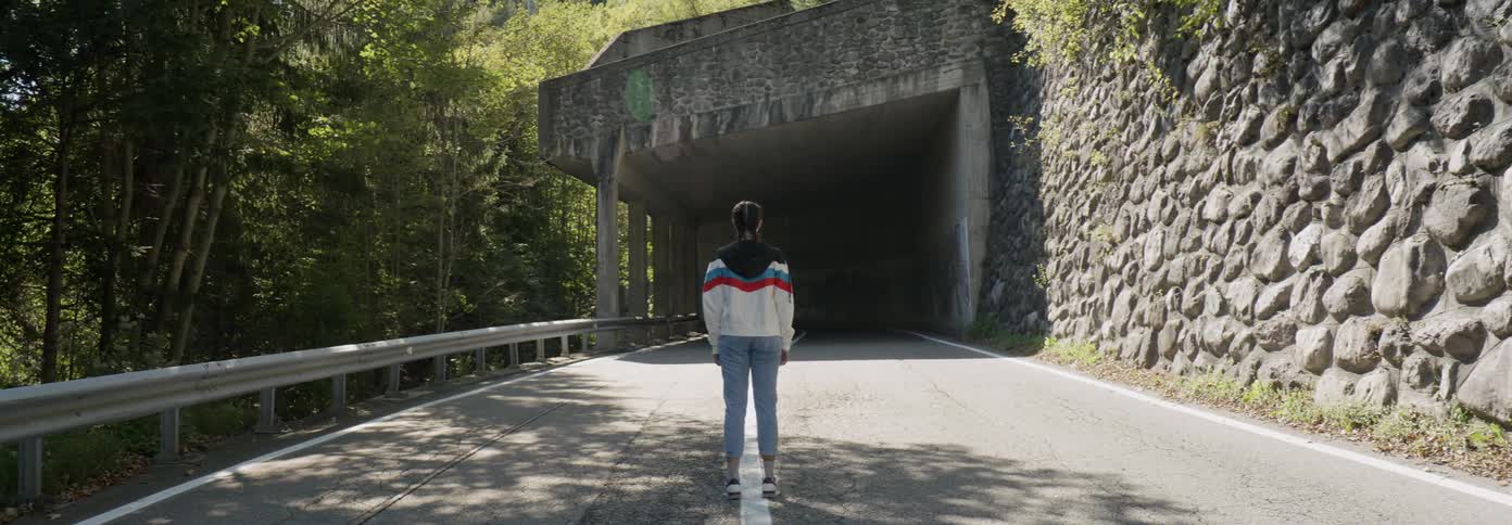 Woman stands in front of a tunnel on a mountain road