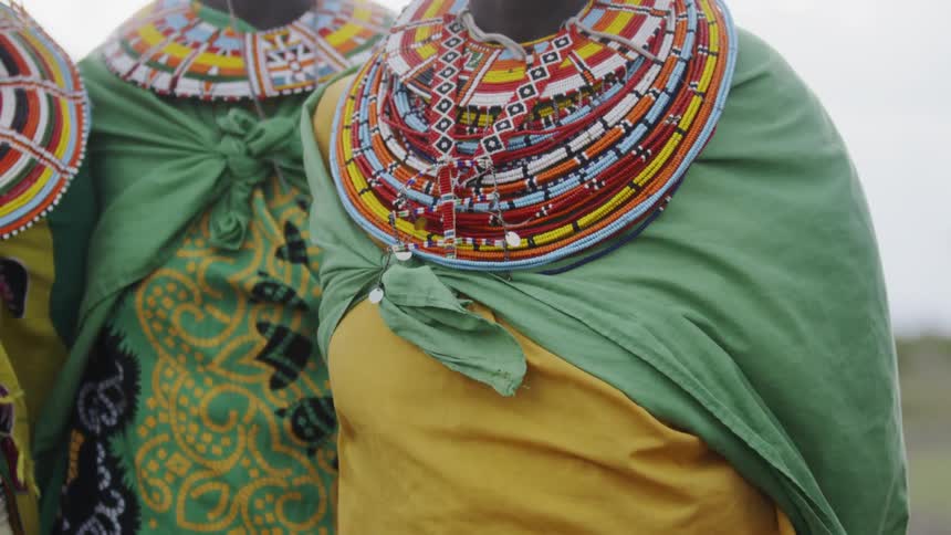 Women in decorated garments stand under a cloudy sky