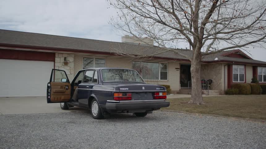 Man gets out of a car parked in front of a house carrying a box