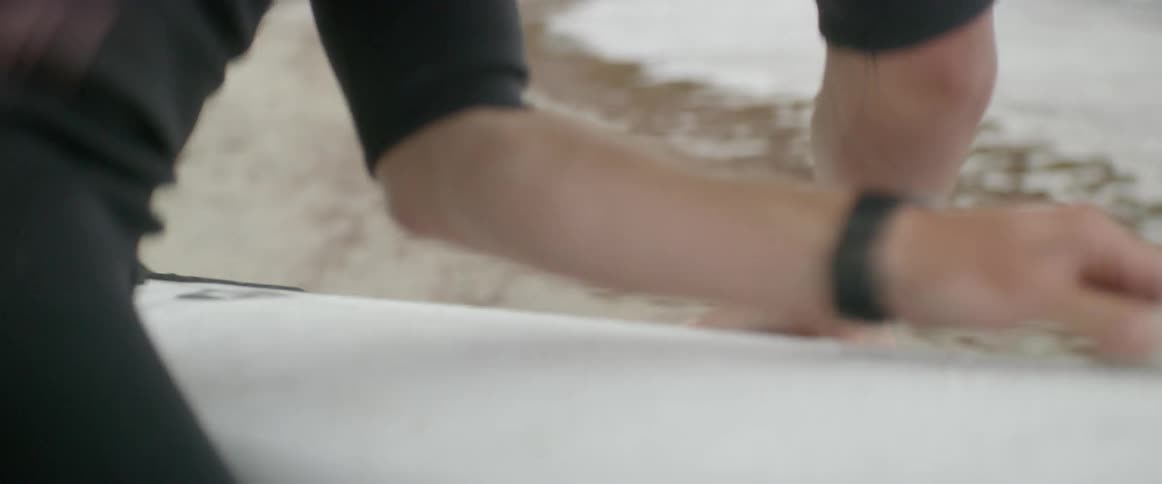 Man carries a surfboard on the beach and rubs it with wax