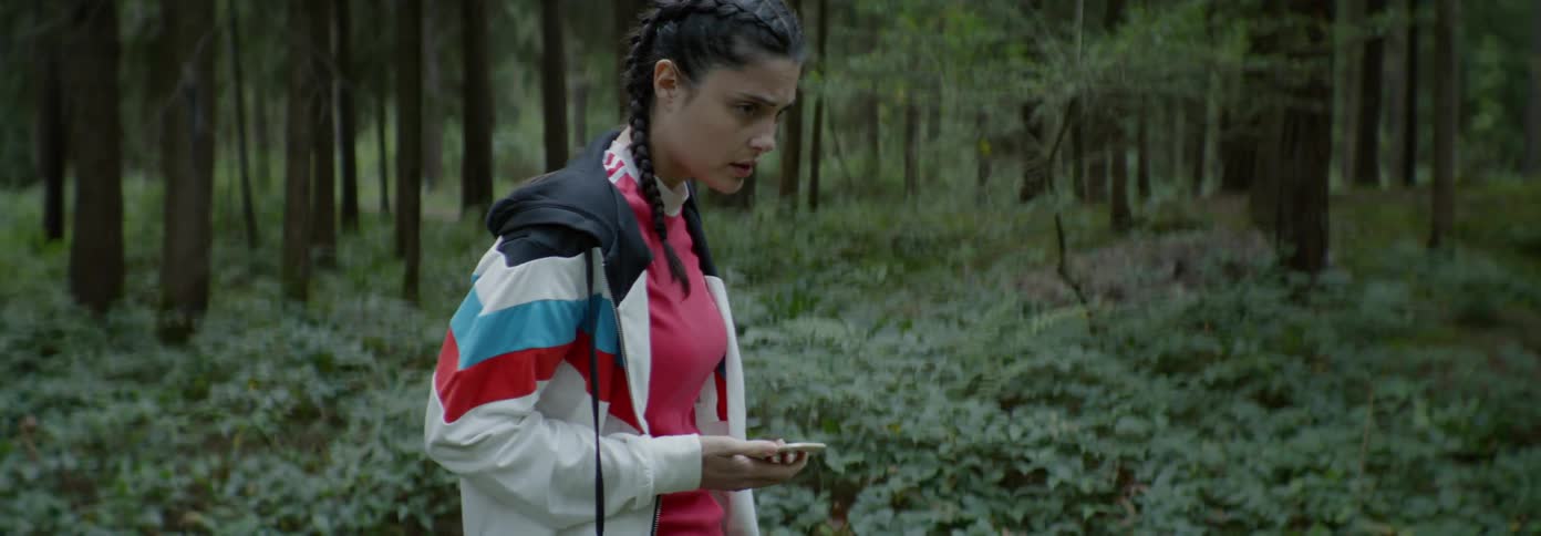 A worried woman looks at her phone in a forest