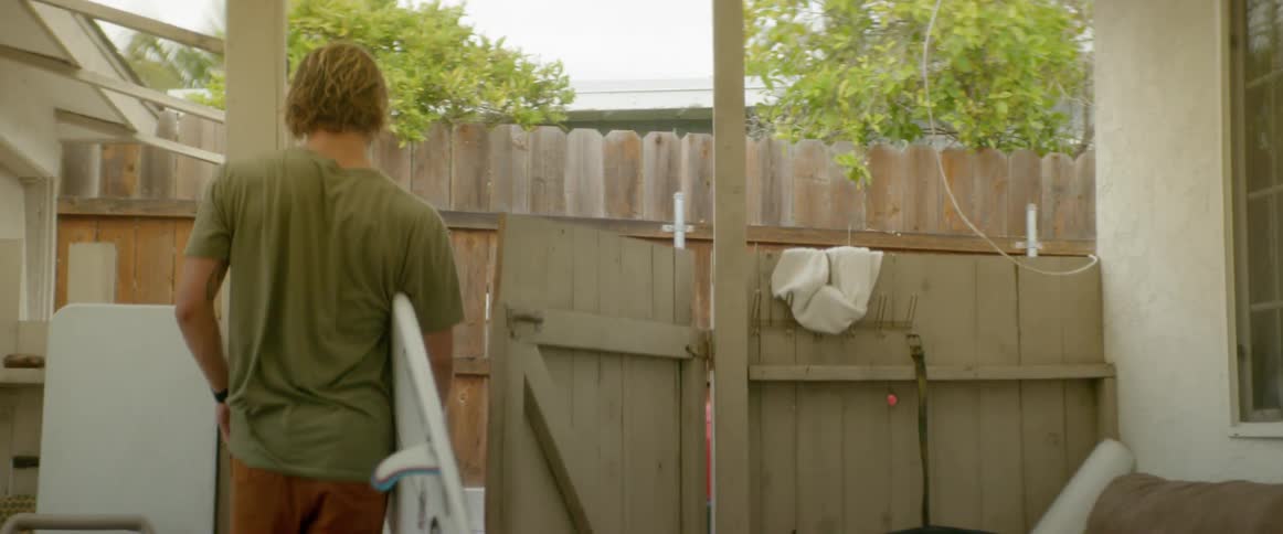 A man exits his yard with his dog and surfboard
