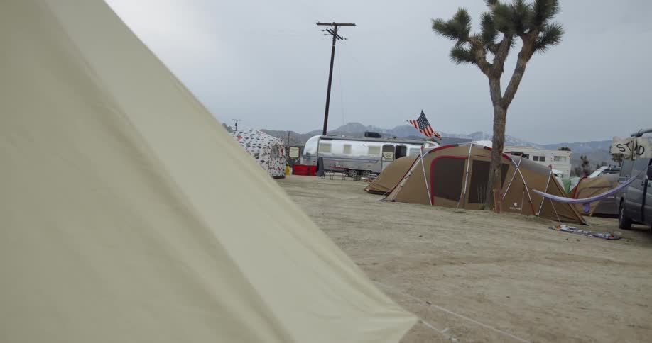 An american flag waves over a tent in a campsite with other tents and a trailer