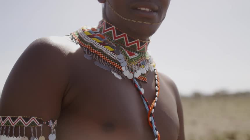 The man is wearing beads and standing shirtless on the field