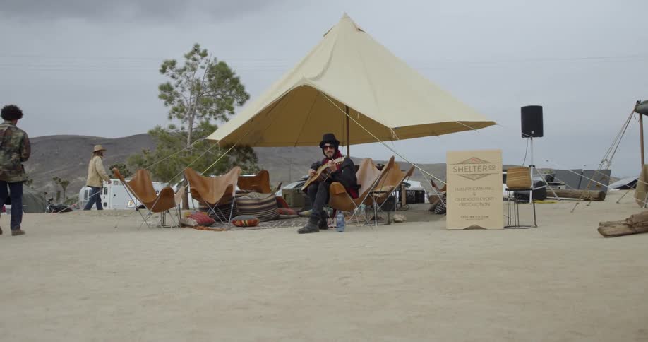 A man sits by the tent playing his guitar