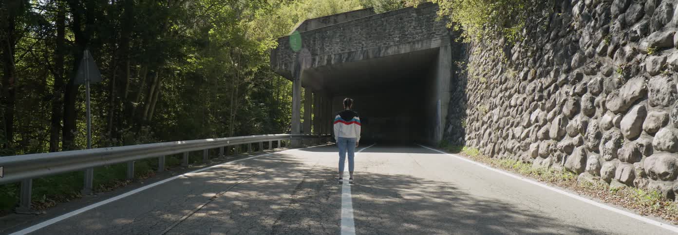 A woman stands on the white line in a road staring at a walled off tunnel