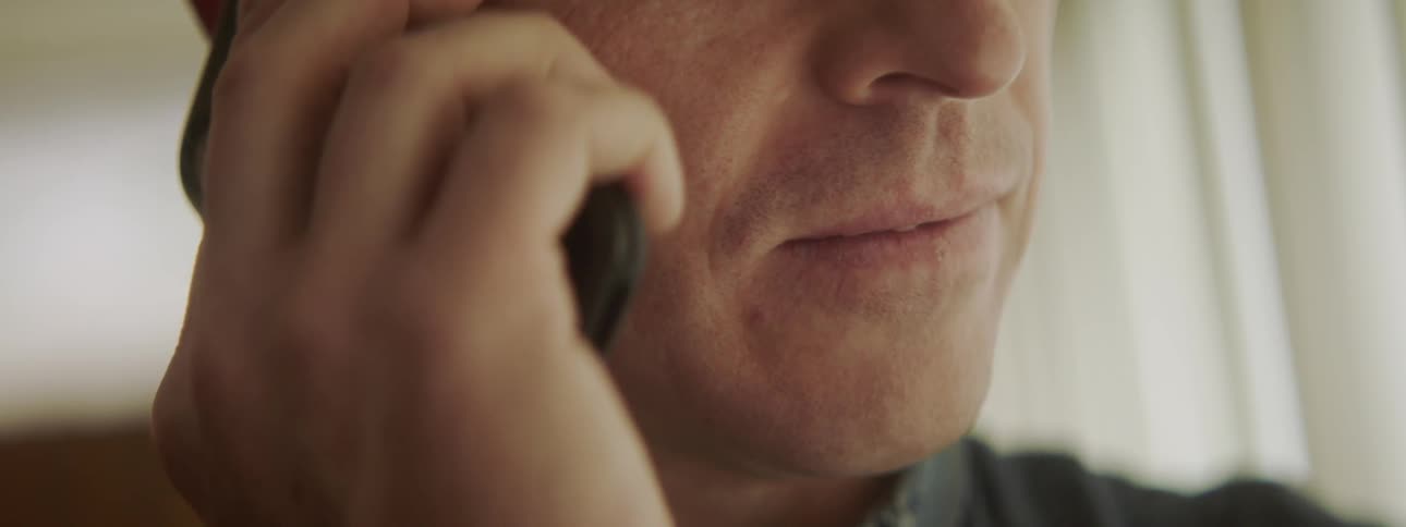 Man talks on a cell phone then rests the phone against his chin