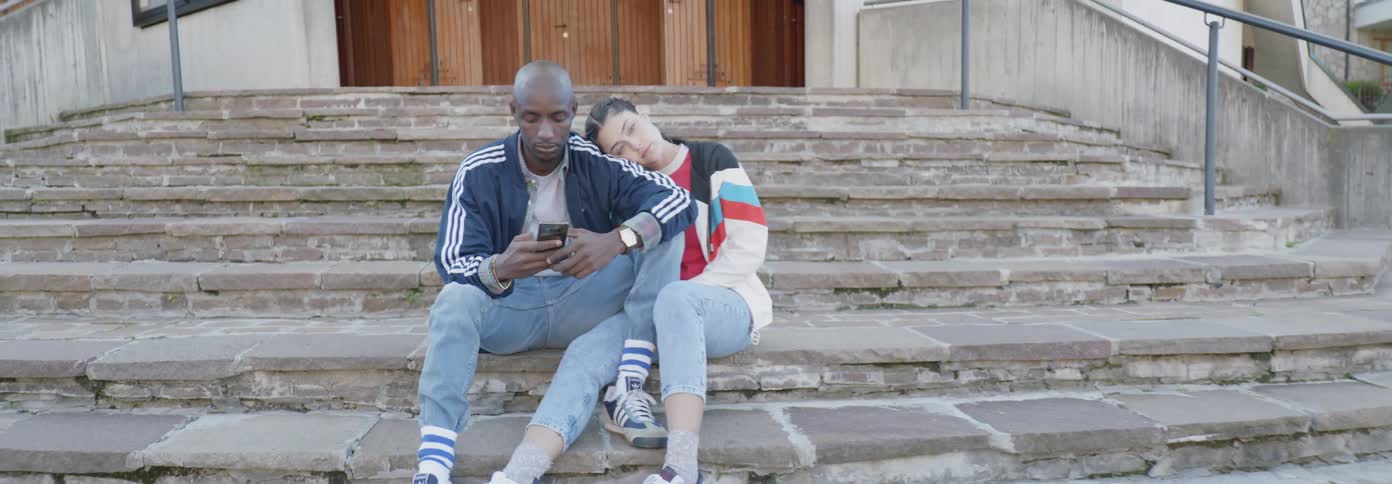 Couple sits on stairs with girl resting and boy texting