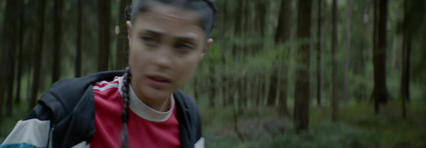 Woman stands in the forest as she looks around in fear