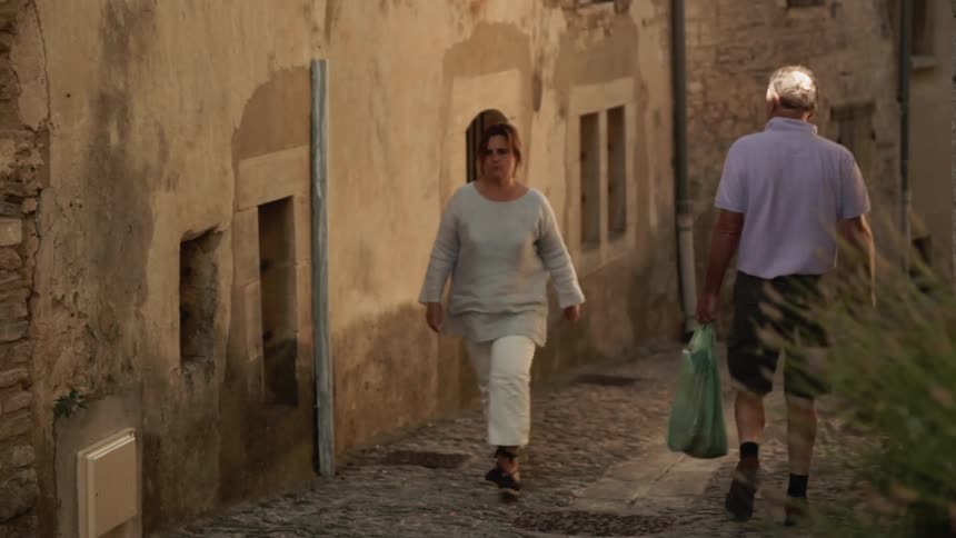 A man carrying a bag passes a woman in the alley