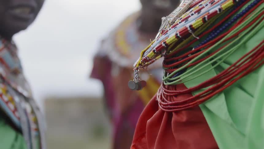 Woman wearing colorful beaded fabric around her neck walks and turns