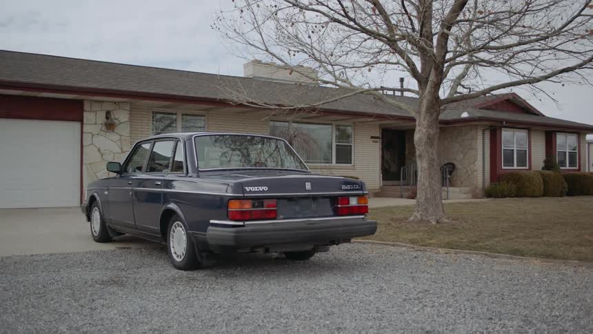 Car sits parked in a driveway near a house and tree
