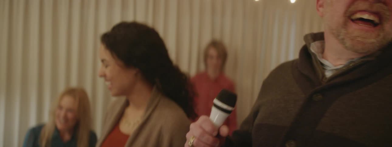 Smiling man holds a microphone and dances at a party